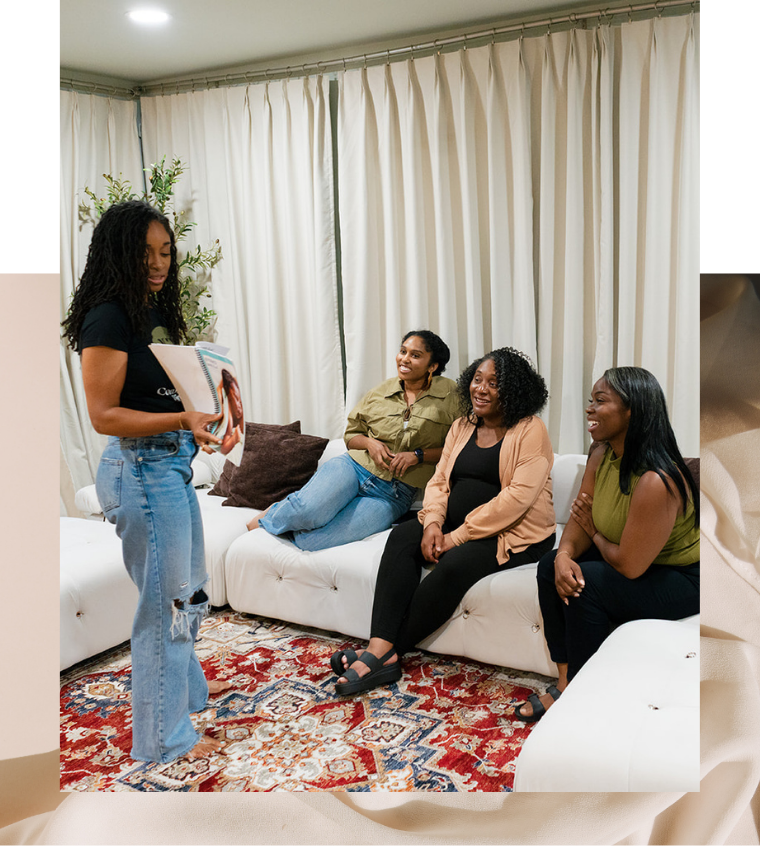 A group of women seated on a plush couch, engaged in conversation, with a patterned rug beneath them and flowing curtains in the background.